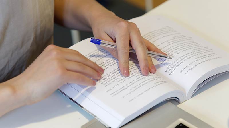 Detaljbild på  händer som håller en bok och en penna